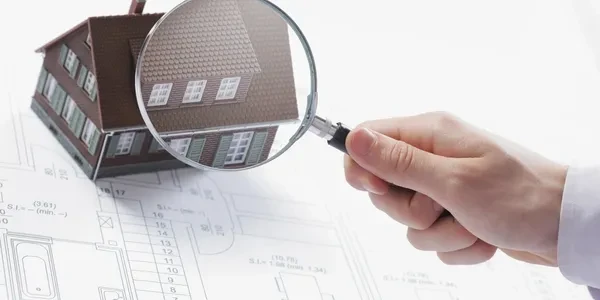 Hand holding magnifying glass over house model on blueprints